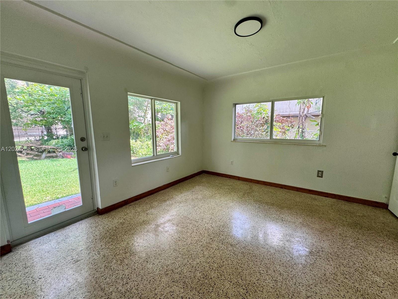 An empty room features white walls, speckled flooring, wood baseboards, and two windows — 8440 NE 1st Ave # 5, Miami FL 33138, MIAMI, FL
