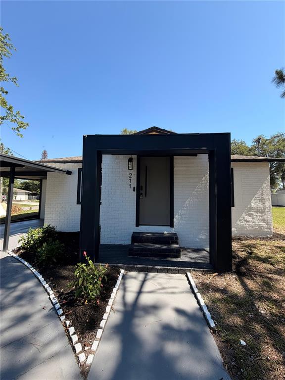 A white brick house features a modern black entryway frame and a concrete walkway — 211 BAYSHORE DRIVE, ORLANDO, FL