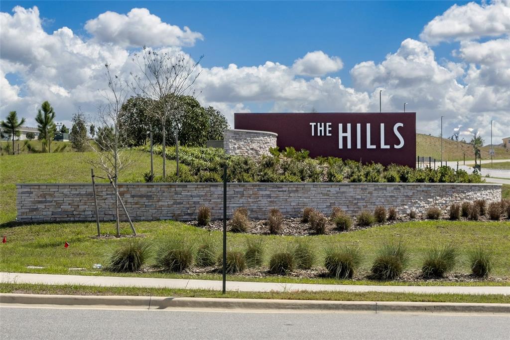 A stone wall and a maroon sign reading The Hills stand in a landscaped area — 2040 SUNSHINE PEAK DRIVE, MINNEOLA, FL