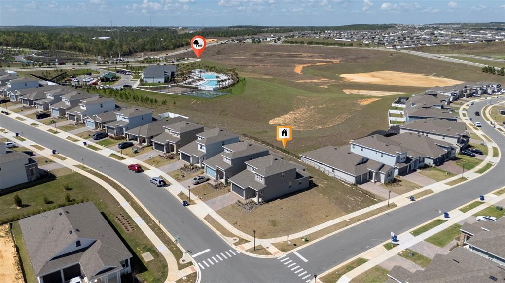 An aerial view shows a suburban neighborhood with houses, a community pool, and undeveloped land — 2040 SUNSHINE PEAK DRIVE, MINNEOLA, FL