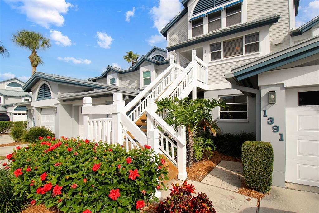A multi-story residential building with white siding, a wooden staircase, and red hibiscus flowers — 1391 SIESTA BAYSIDE DRIVE UNIT 1391-B, SARASOTA, FL