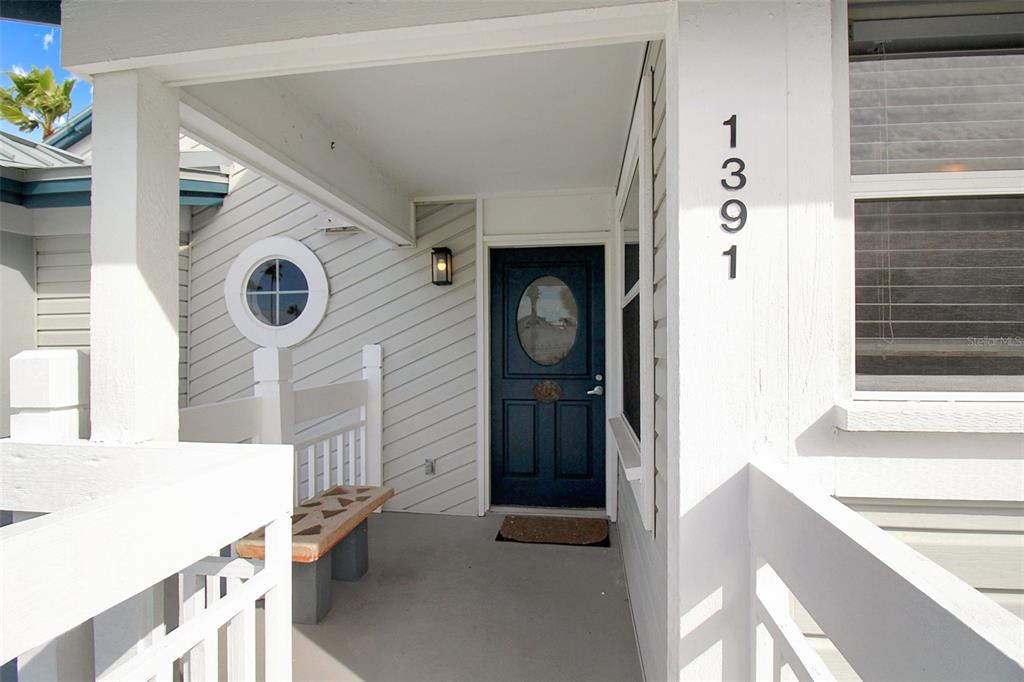 A covered porch features a dark blue front door, a small bench, and white siding — 1391 SIESTA BAYSIDE DRIVE UNIT 1391-B, SARASOTA, FL