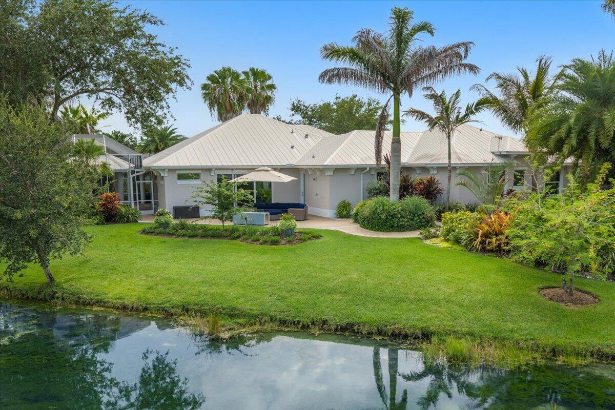 A single-story house with a metal roof sits behind a grassy lawn and a pond — VERO BEACH, FL