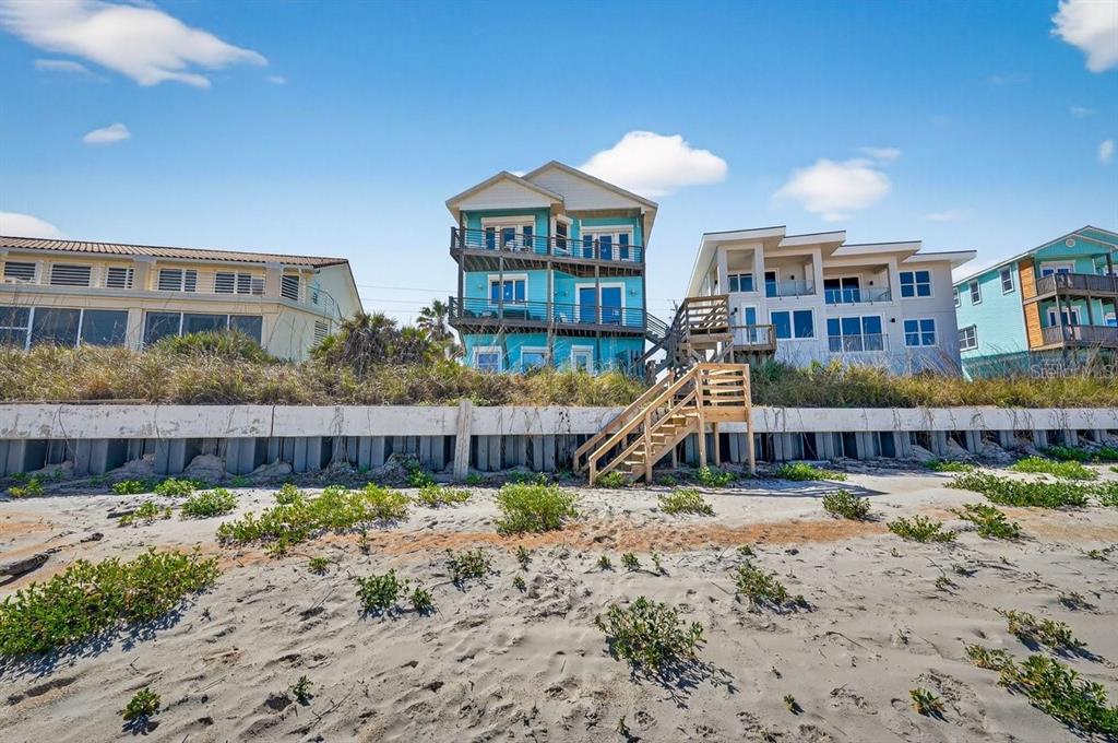 A view from the beach looking up at three multi-story houses behind a concrete seawall — 3319 N OCEAN SHORE BOULEVARD, FLAGLER BEACH, FL