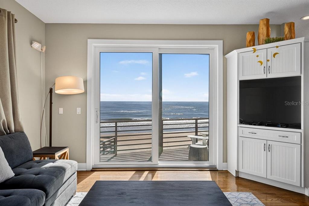 A living room features a dark sofa, a television cabinet, and sliding doors overlooking the ocean — 3319 N OCEAN SHORE BOULEVARD, FLAGLER BEACH, FL