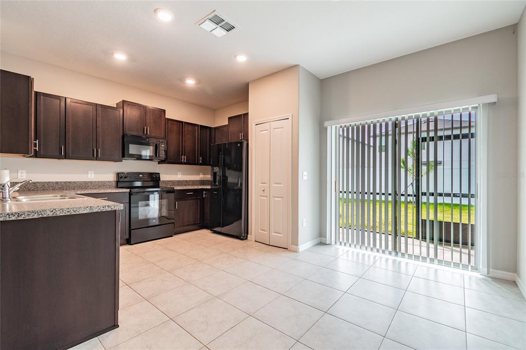 A kitchen features dark wood cabinets, black appliances, granite countertops, and a sliding glass door — 7221 SWEET ALYSSUM COURT, TAMPA, FL