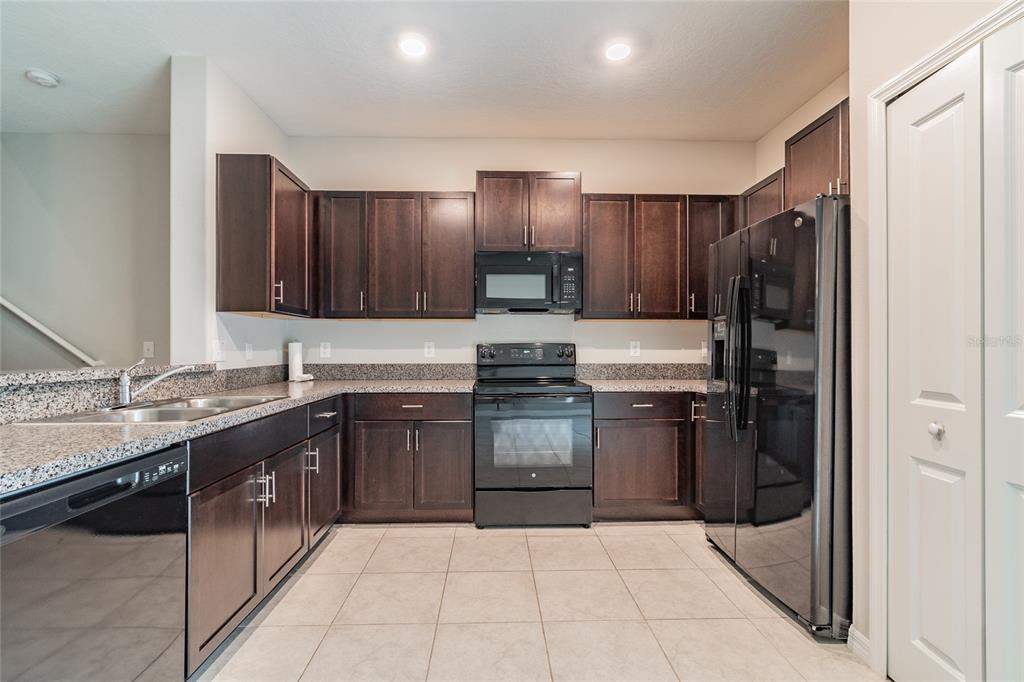 A kitchen features dark wood cabinets, granite countertops, and black appliances on a tiled floor — 7221 SWEET ALYSSUM COURT, TAMPA, FL