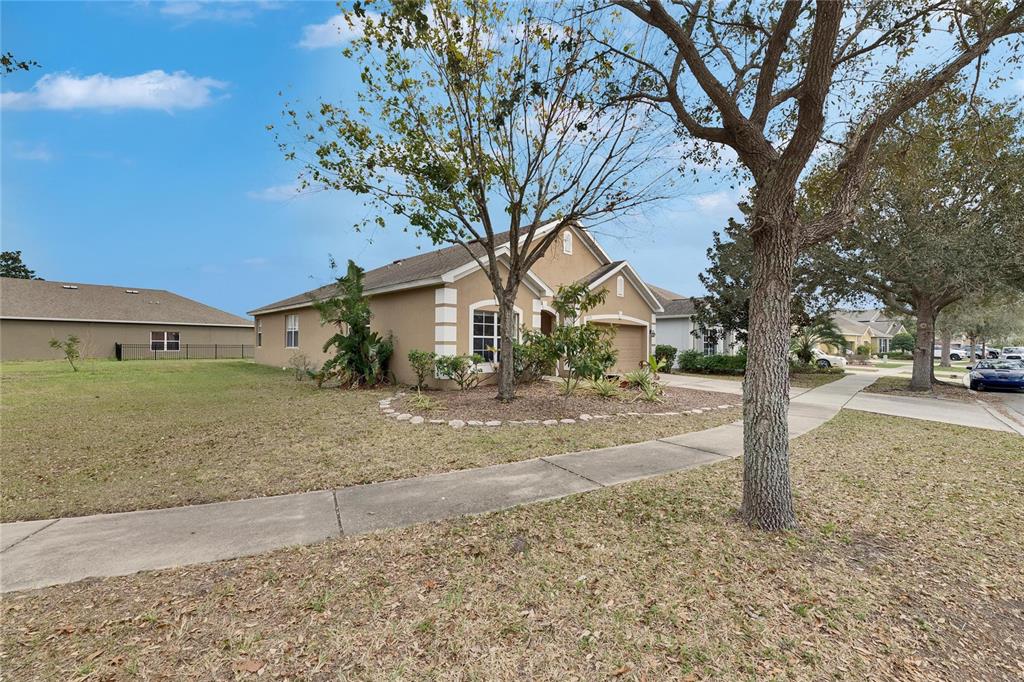 A tan single-story house with a garage and a landscaped front yard under a blue sky — 10328 CELTIC ASH DRIVE, RUSKIN, FL
