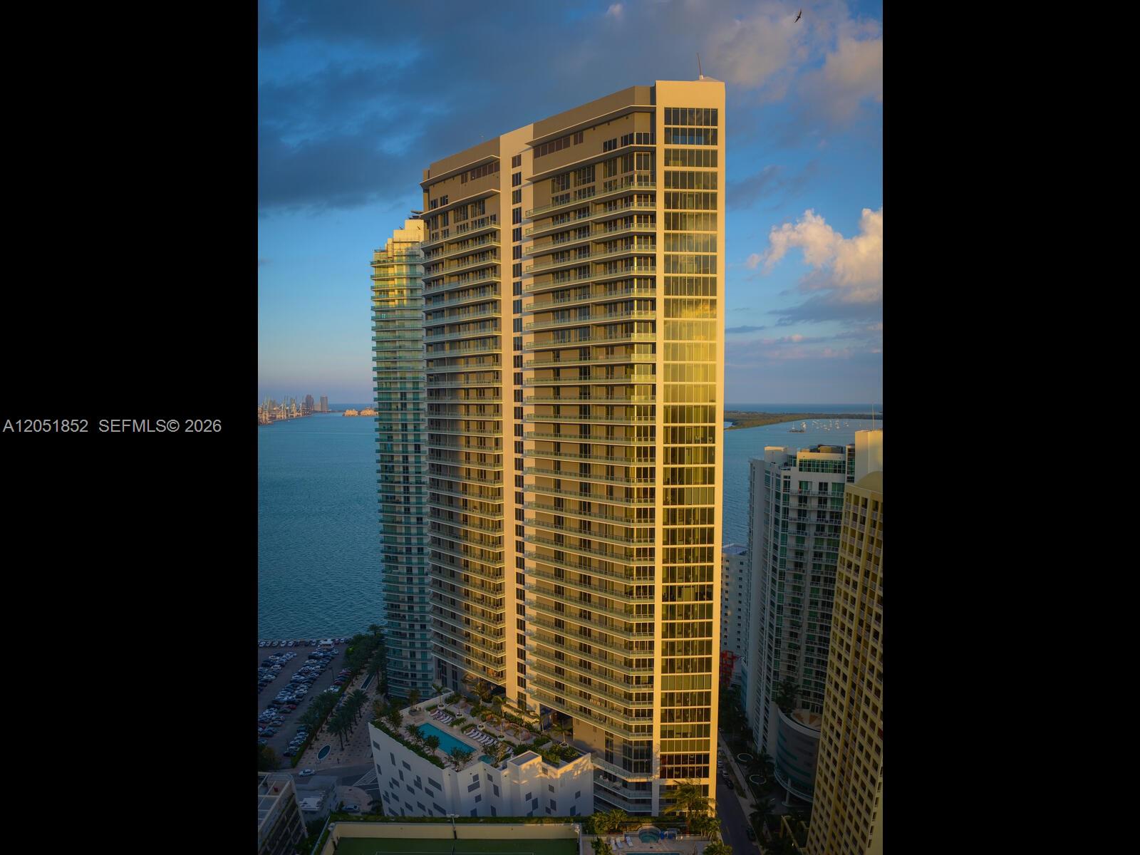 An aerial view of a tall residential skyscraper overlooking a bay at sunset — 1300 Brickell Bay Dr # 3804, Miami FL 33131, MIAMI, FL