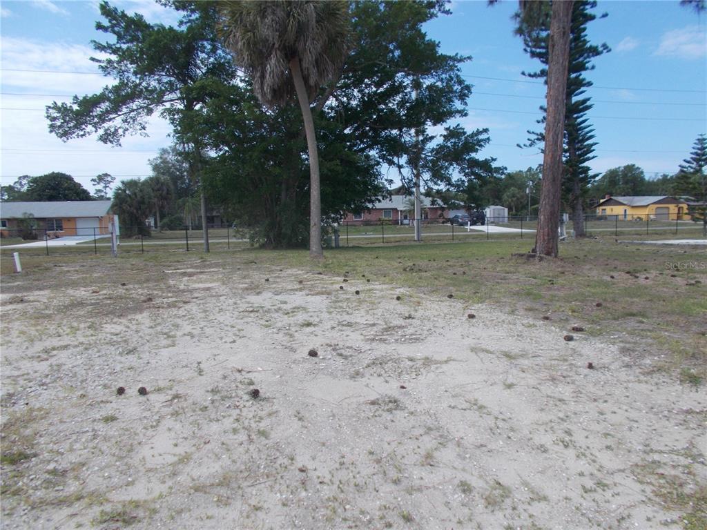 A flat, sandy residential lot with scattered pine cones and mature trees in the background — 5090 PALENA BOULEVARD, NORTH PORT, FL