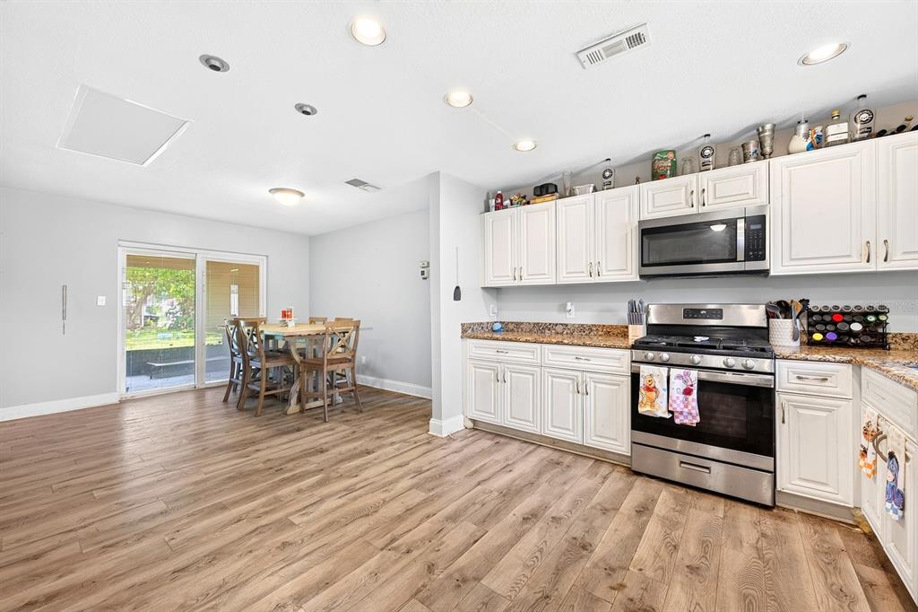 A kitchen with white cabinets, stainless steel appliances, and wood-look flooring opens to a dining area — 10330 LICORICE WAY, ORLANDO, FL