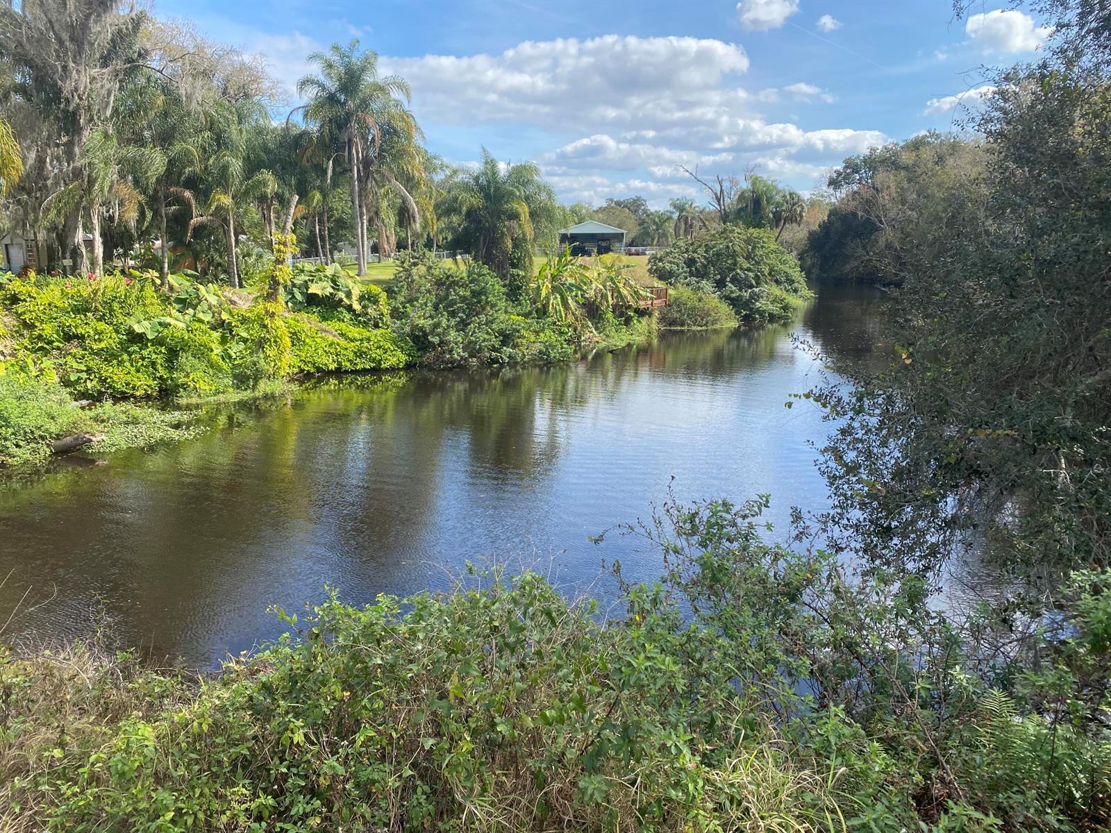 A calm river flows through a lush, green landscape with palm trees and a small building — 1055 Lake Josephine Drive, Sebring FL 33875, SEBRING, FL