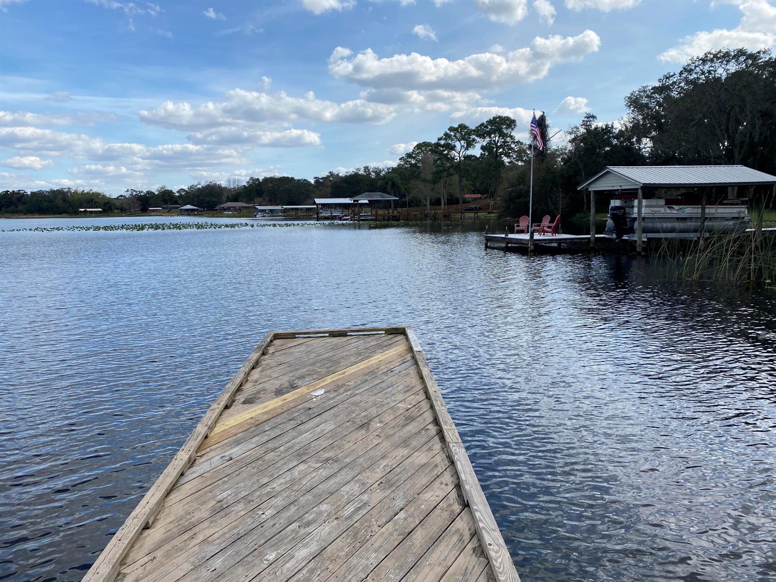 A wooden dock extends into a lake with a boat slip and flag nearby — 1055 Lake Josephine Drive, Sebring FL 33875, SEBRING, FL