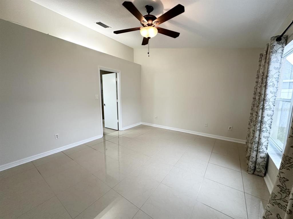 A bedroom with light-colored tile flooring, beige walls, a ceiling fan, and a doorway — 931 HUNTER LANE, TARPON SPRINGS, FL