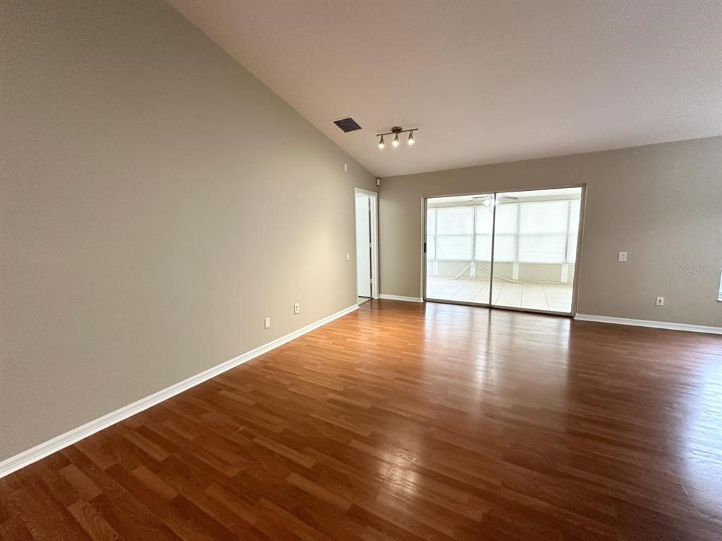 An empty living room features hardwood flooring, a vaulted ceiling, and sliding glass doors — 931 HUNTER LANE, TARPON SPRINGS, FL