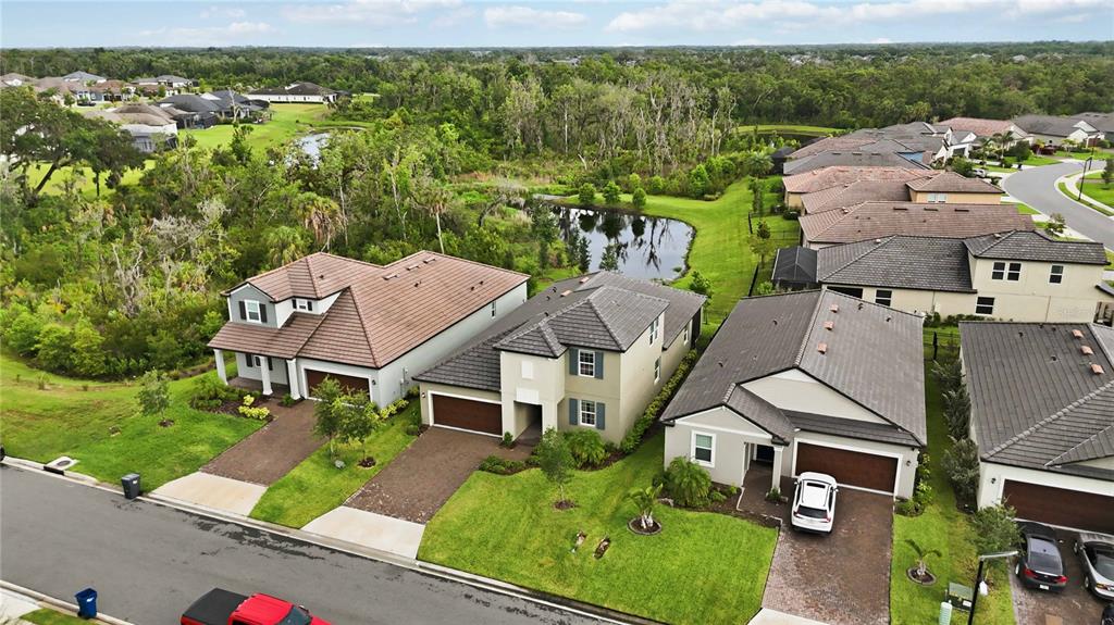 An aerial view shows three suburban houses with tiled roofs and driveways near a pond — 14325 17TH COURT E, PARRISH, FL