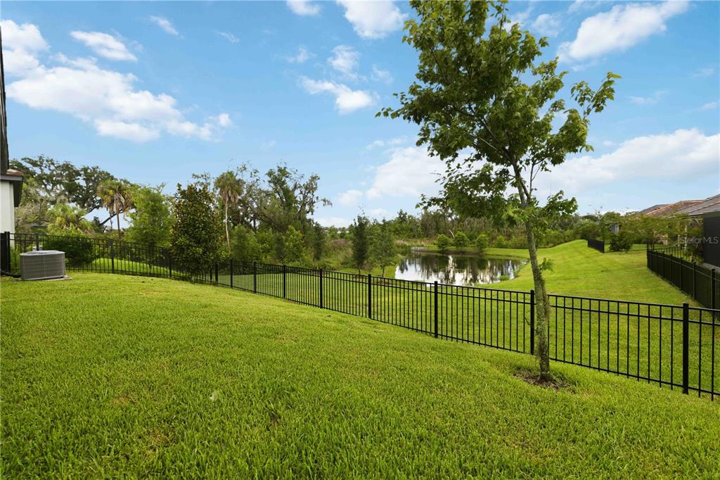A grassy backyard features a black metal fence, a small pond, and scattered trees — 14325 17TH COURT E, PARRISH, FL