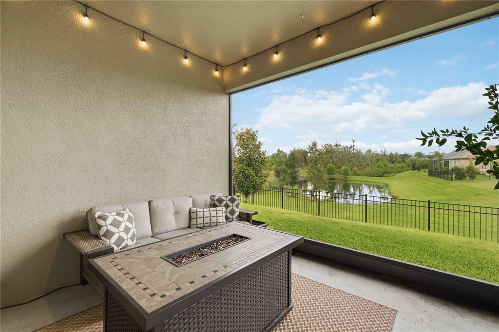 A covered patio features a fire pit table, outdoor sofa, and a view of a pond — 14325 17TH COURT E, PARRISH, FL