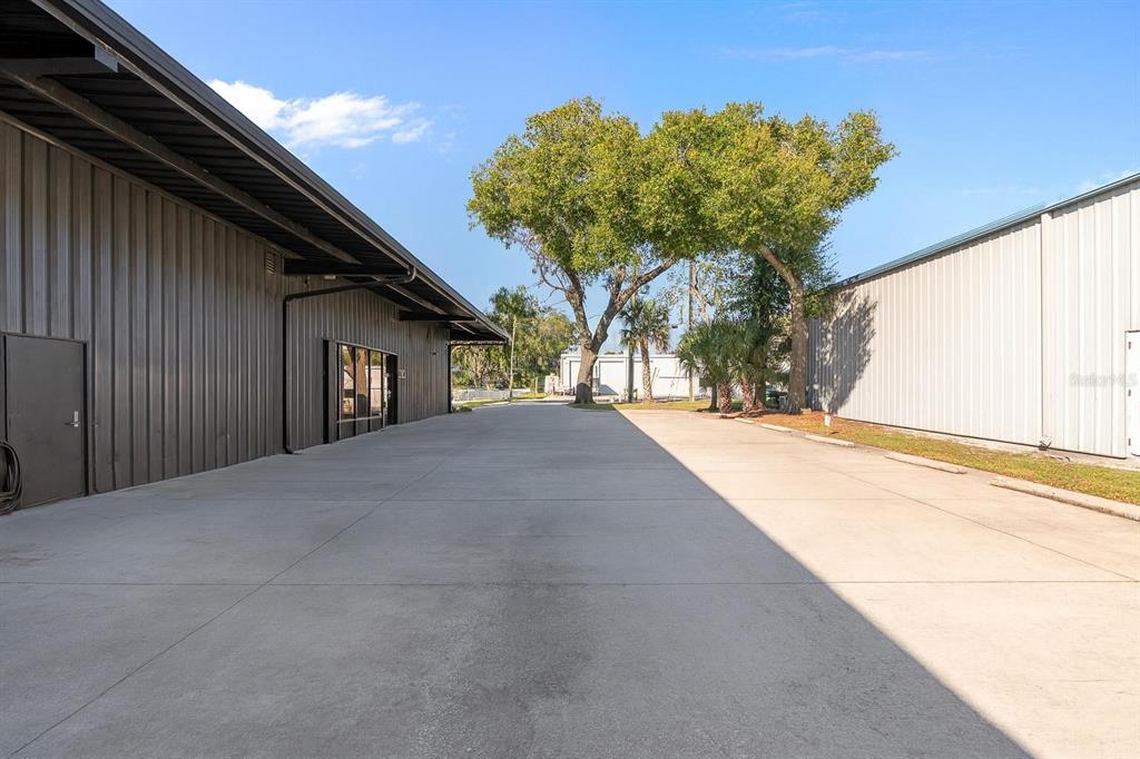 A concrete driveway sits between two industrial metal buildings under a clear blue sky — 210 E PALMETTO AVENUE, LONGWOOD, FL