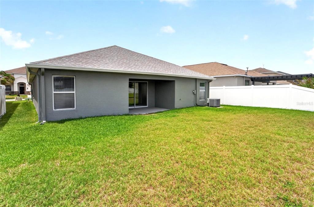 The exterior rear view of a gray house features a small patio and grassy yard — 13128 ROYAL PINES AVENUE, RIVERVIEW, FL