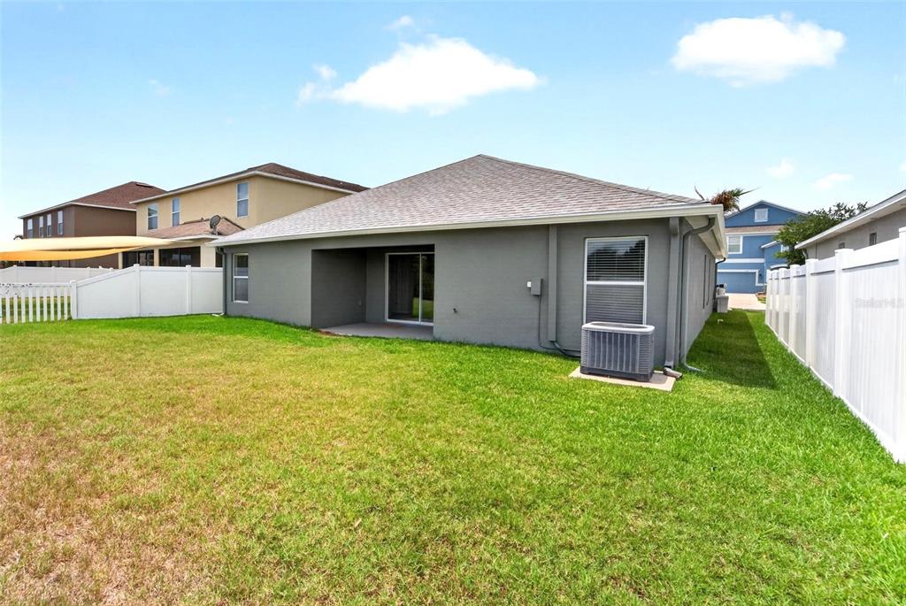 The backyard of a gray house features a covered patio, lawn, and white vinyl fencing — 13128 ROYAL PINES AVENUE, RIVERVIEW, FL