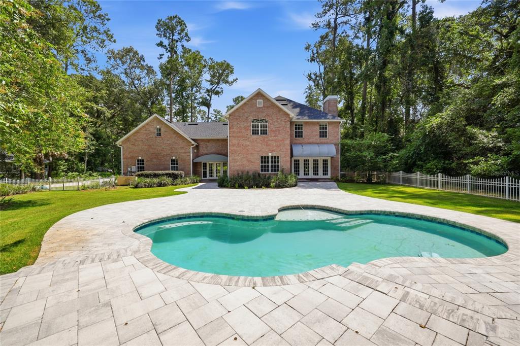 An aerial view shows a brick house with a pool and patio surrounded by trees — 11121 NW 15TH PLACE, GAINESVILLE, FL