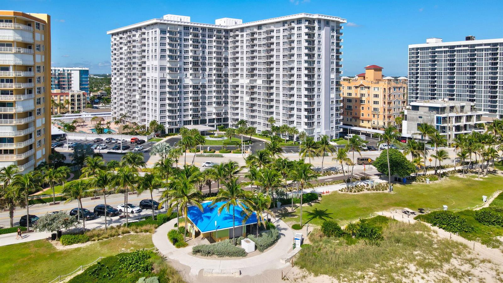 An aerial view shows a large white apartment building near a beach with palm trees — 405 N Ocean Boulevard # 329, Pompano Beach FL 33062, POMPANO BEACH, FL