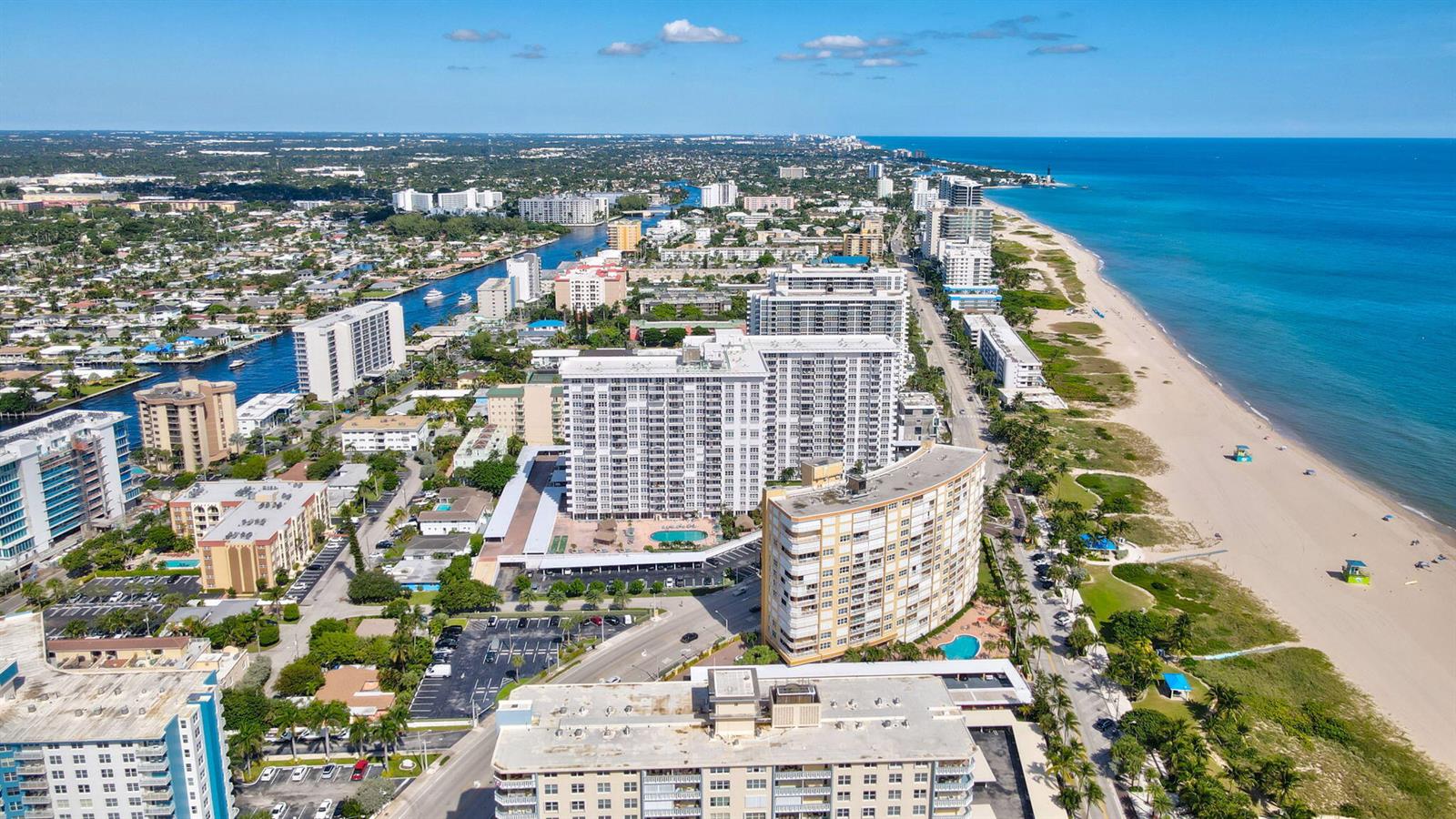 An aerial view shows high-rise apartment buildings along a sandy beach and a coastal waterway — 405 N Ocean Boulevard # 329, Pompano Beach FL 33062, POMPANO BEACH, FL