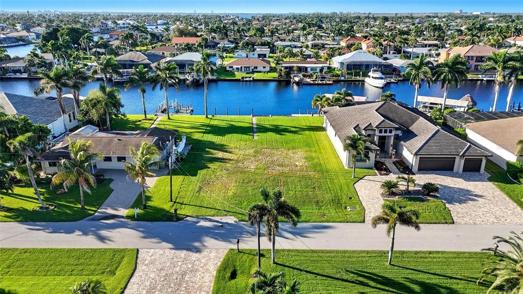 An aerial view shows a vacant waterfront lot situated between two residential homes — 126 SW 50TH STREET, CAPE CORAL, FL