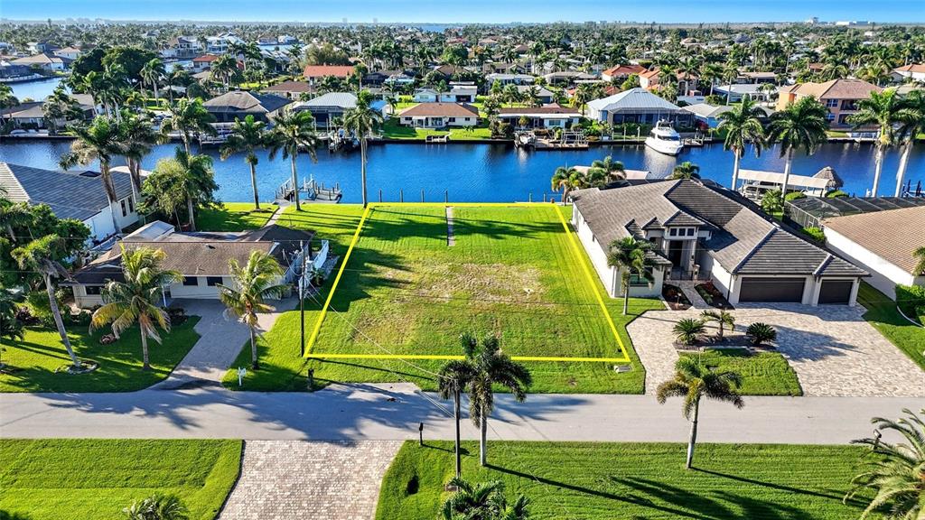 An aerial view shows a vacant waterfront lot situated between two residential houses — 126 SW 50TH STREET, CAPE CORAL, FL