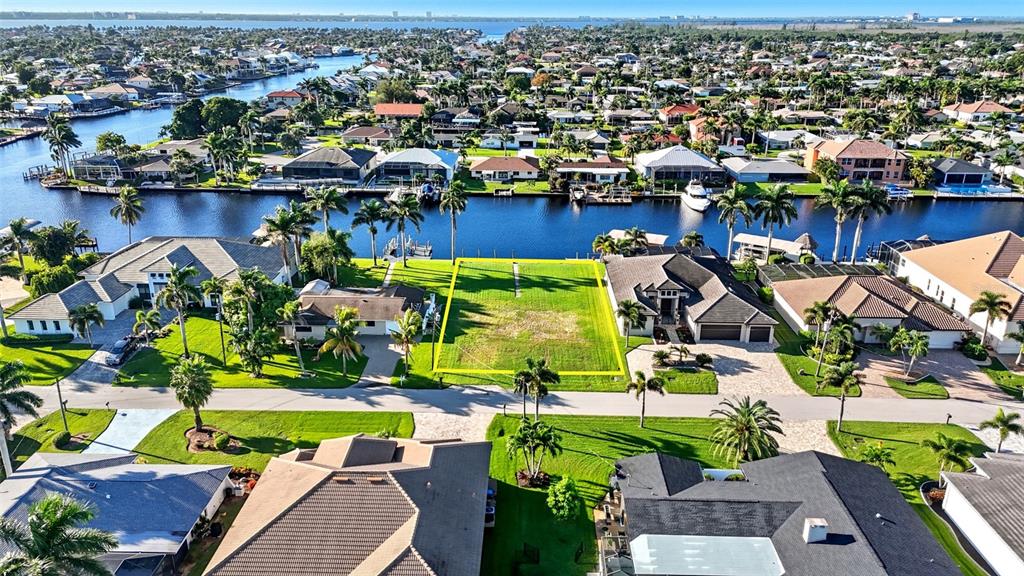 An aerial view shows a vacant residential lot outlined in yellow between two houses — 126 SW 50TH STREET, CAPE CORAL, FL