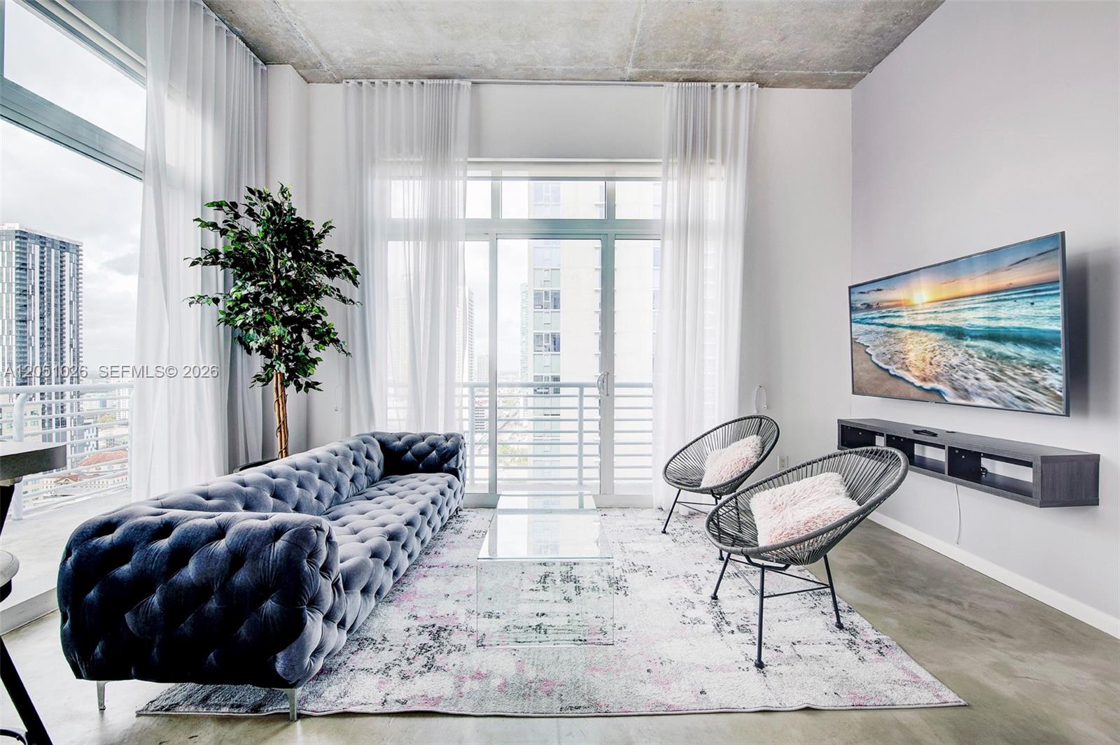 A modern living room features a tufted gray sofa, two wire chairs, and a wall-mounted television — 234 NE 3rd St, Miami FL 33132, MIAMI, FL