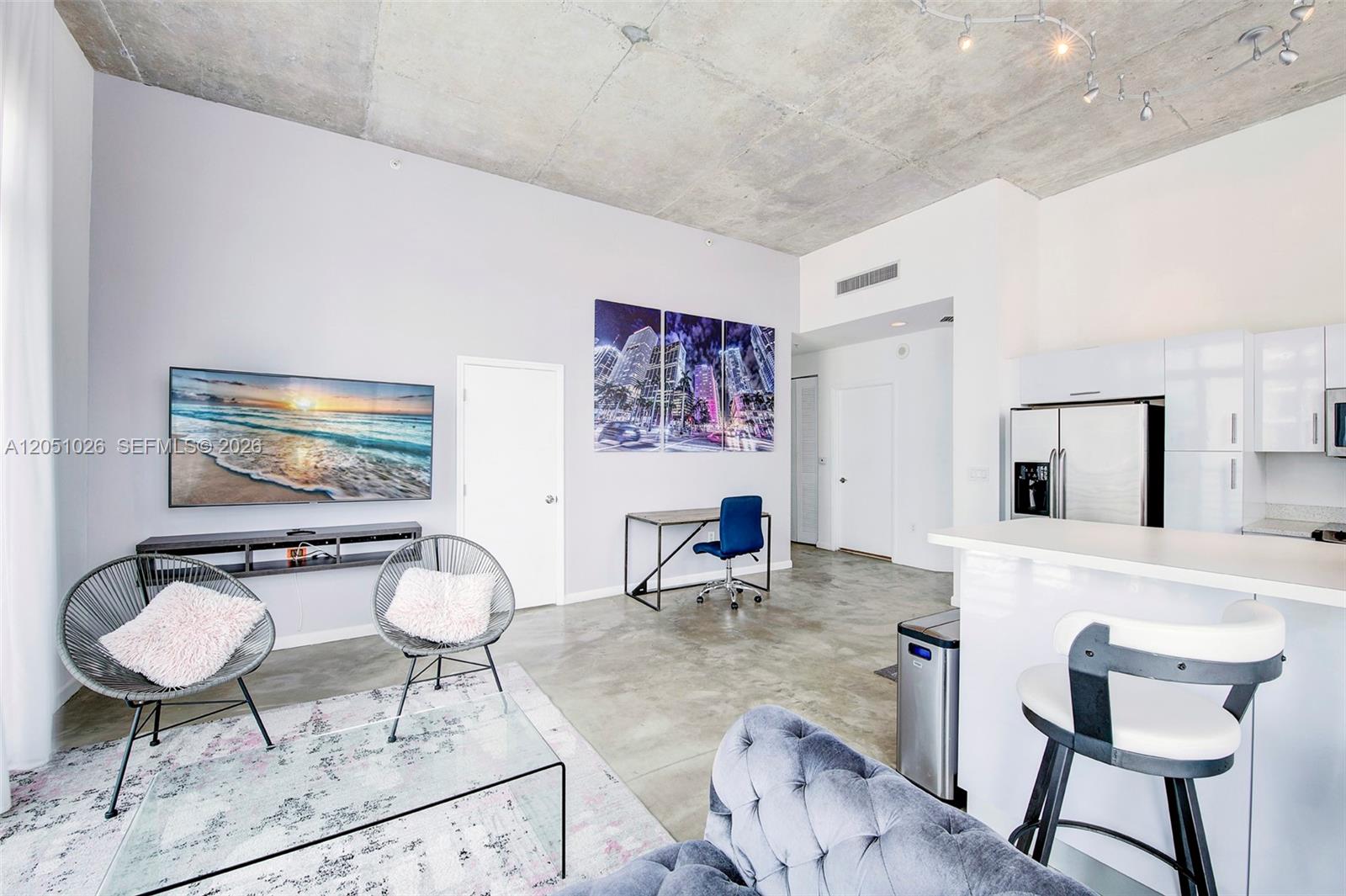 A modern living room features concrete ceilings, white walls, and an open kitchen area — 234 NE 3rd St, Miami FL 33132, MIAMI, FL