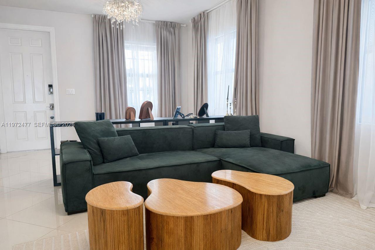 A living room features a dark green sectional sofa, three wooden coffee tables, and curtains — 829 NE 191st St, Miami FL 33179, MIAMI, FL