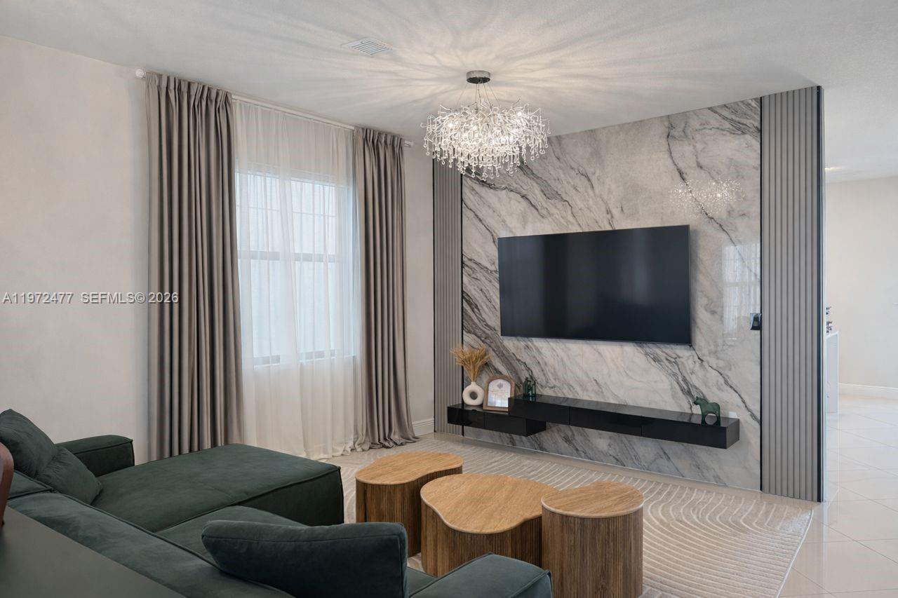 A living room features a marble accent wall with a mounted television and chandelier — 829 NE 191st St, Miami FL 33179, MIAMI, FL