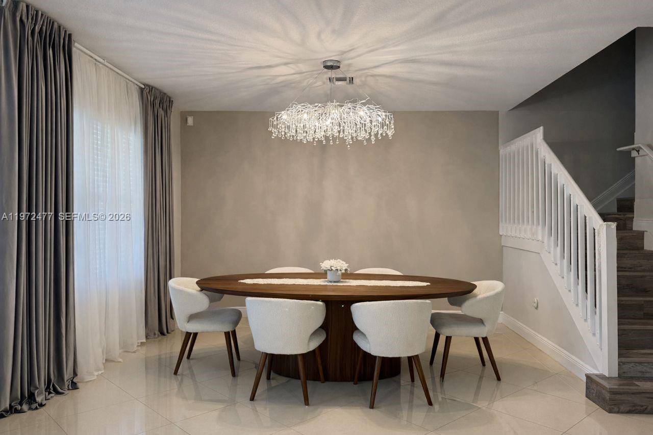 A dining room features a round wooden table, white chairs, and a crystal chandelier — 829 NE 191st St, Miami FL 33179, MIAMI, FL