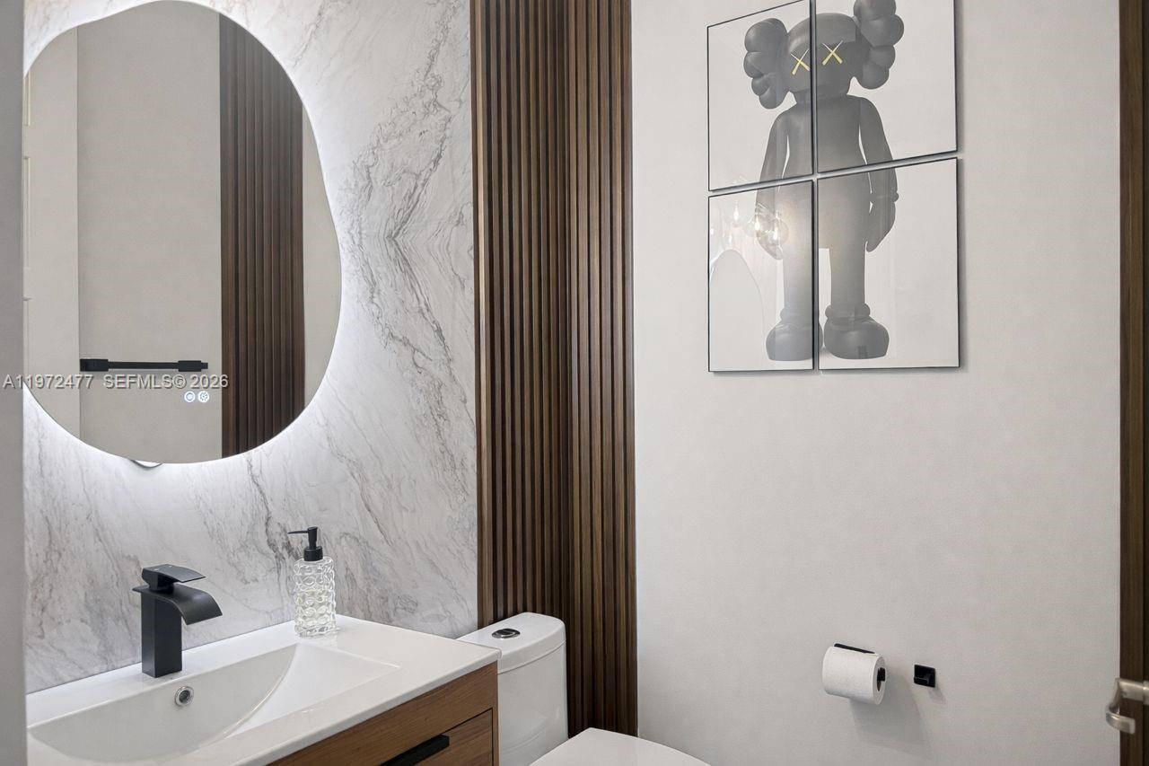 A modern bathroom features a marble-tiled wall, a backlit mirror, and KAWS-style wall art — 829 NE 191st St, Miami FL 33179, MIAMI, FL