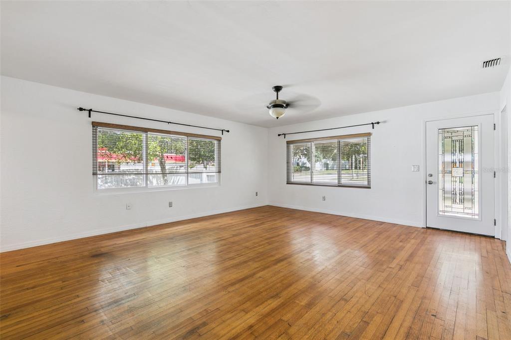 An empty living room features white walls, hardwood floors, two windows, and a ceiling fan — 1652 BERKSHIRE AVENUE, WINTER PARK, FL