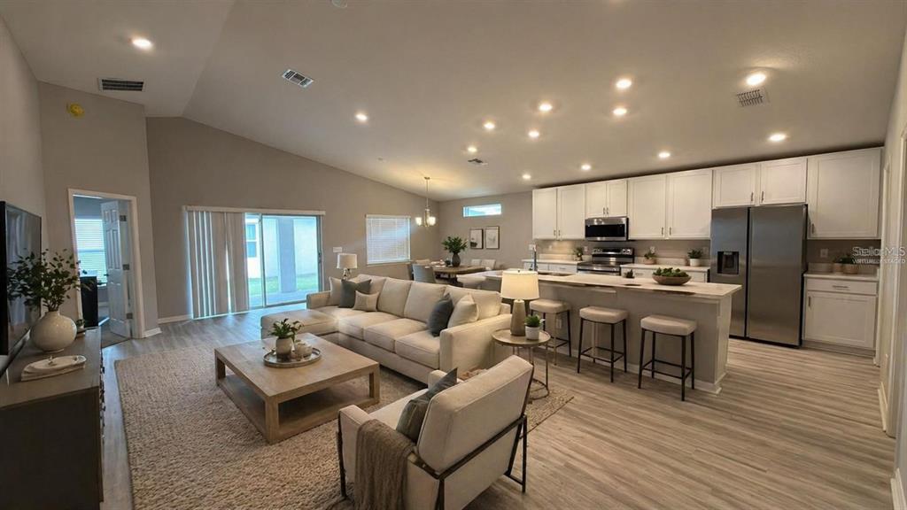 This open-concept living room and kitchen features white cabinetry, stainless appliances, and light wood flooring — 485 WINDY WILLOW WAY, ST CLOUD, FL