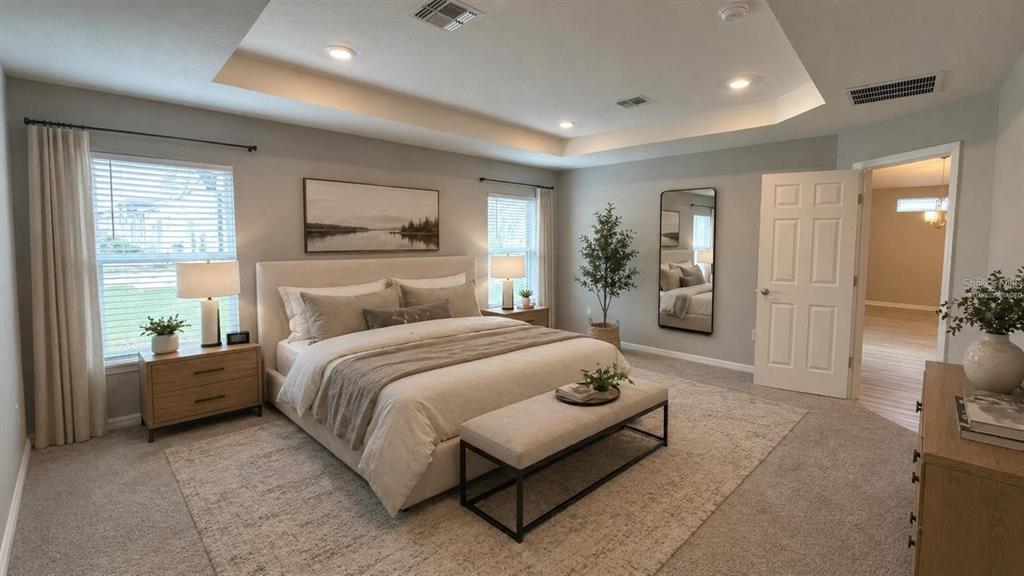 A bedroom features a tray ceiling, a king-sized bed, a bench, and neutral decor — 485 WINDY WILLOW WAY, ST CLOUD, FL