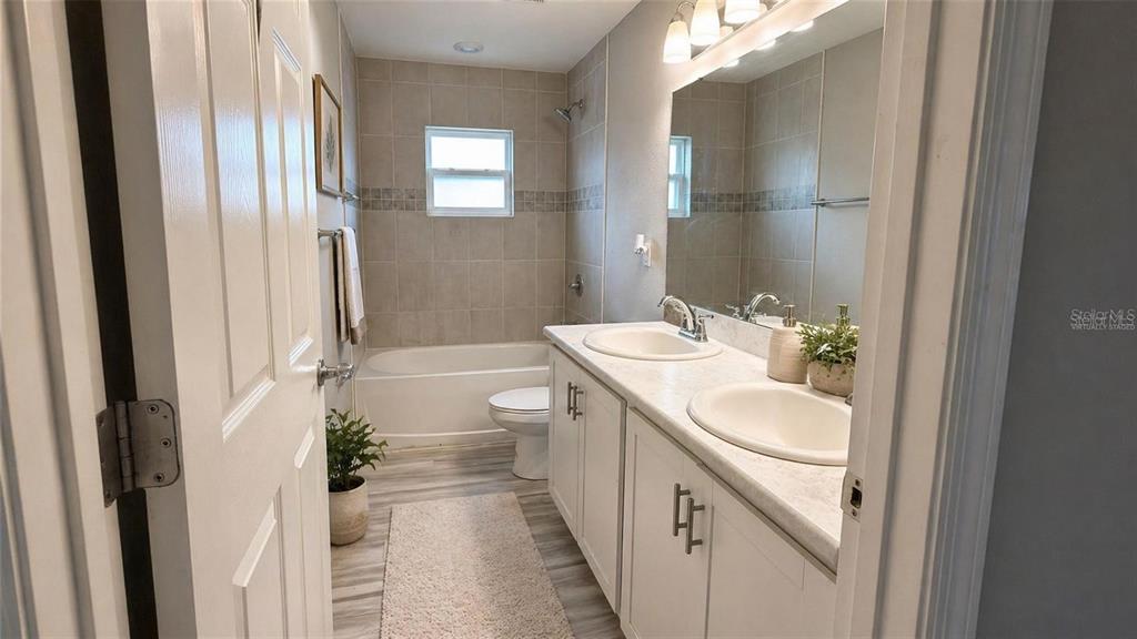 A bathroom features a double vanity with white cabinets, a tub-shower combination, and tiled walls — 485 WINDY WILLOW WAY, ST CLOUD, FL