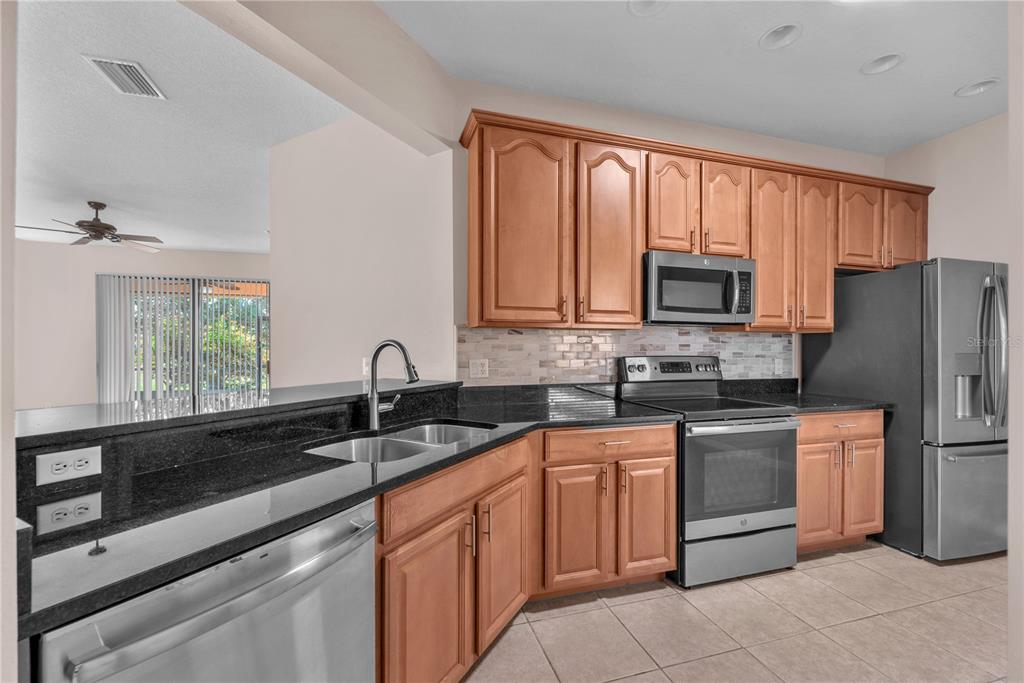 A kitchen with wood cabinets, black countertops, stainless steel appliances, and a tiled floor — 107 SHELL FALLS DRIVE, APOLLO BEACH, FL
