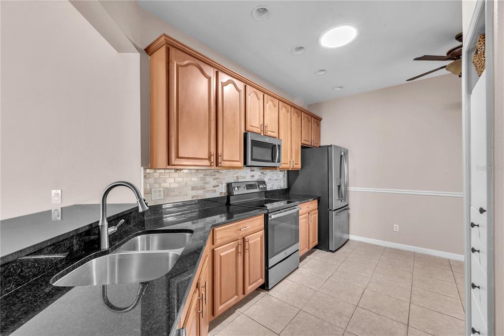 A kitchen features wood cabinets, black granite countertops, stainless steel appliances, and tile flooring — 107 SHELL FALLS DRIVE, APOLLO BEACH, FL