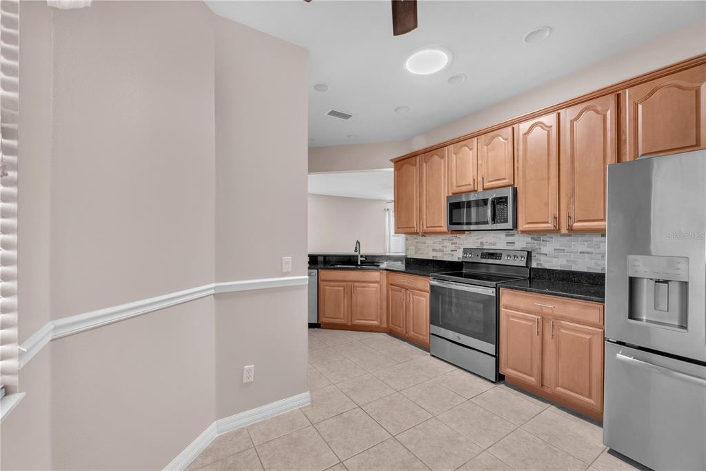 A kitchen features light wood cabinets, dark granite countertops, stainless steel appliances, and tile flooring — 107 SHELL FALLS DRIVE, APOLLO BEACH, FL