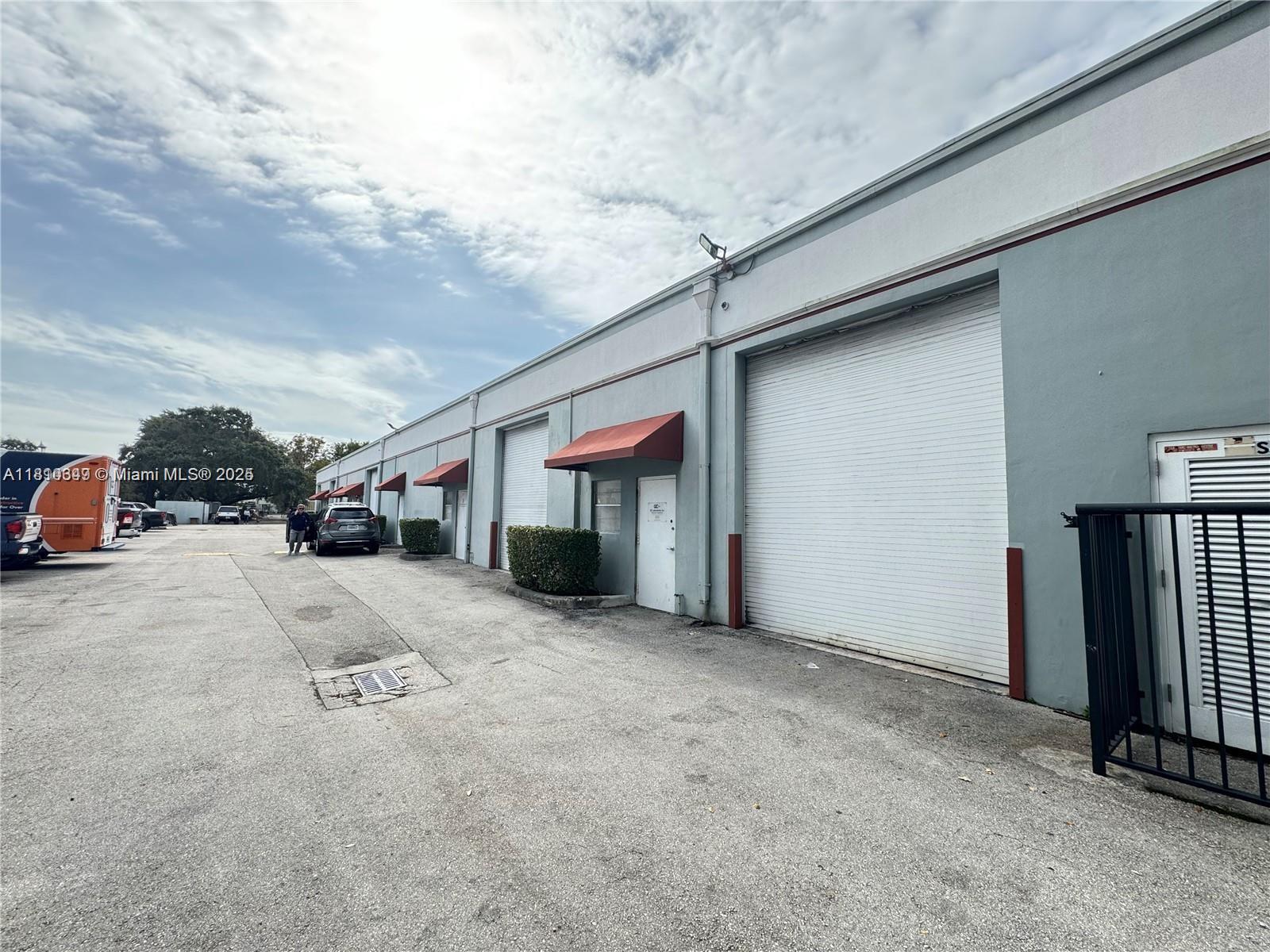An exterior view of a commercial warehouse building with multiple roll-up doors and red awnings — 2870 Stirling Rd, Hollywood FL 33020, HOLLYWOOD, FL