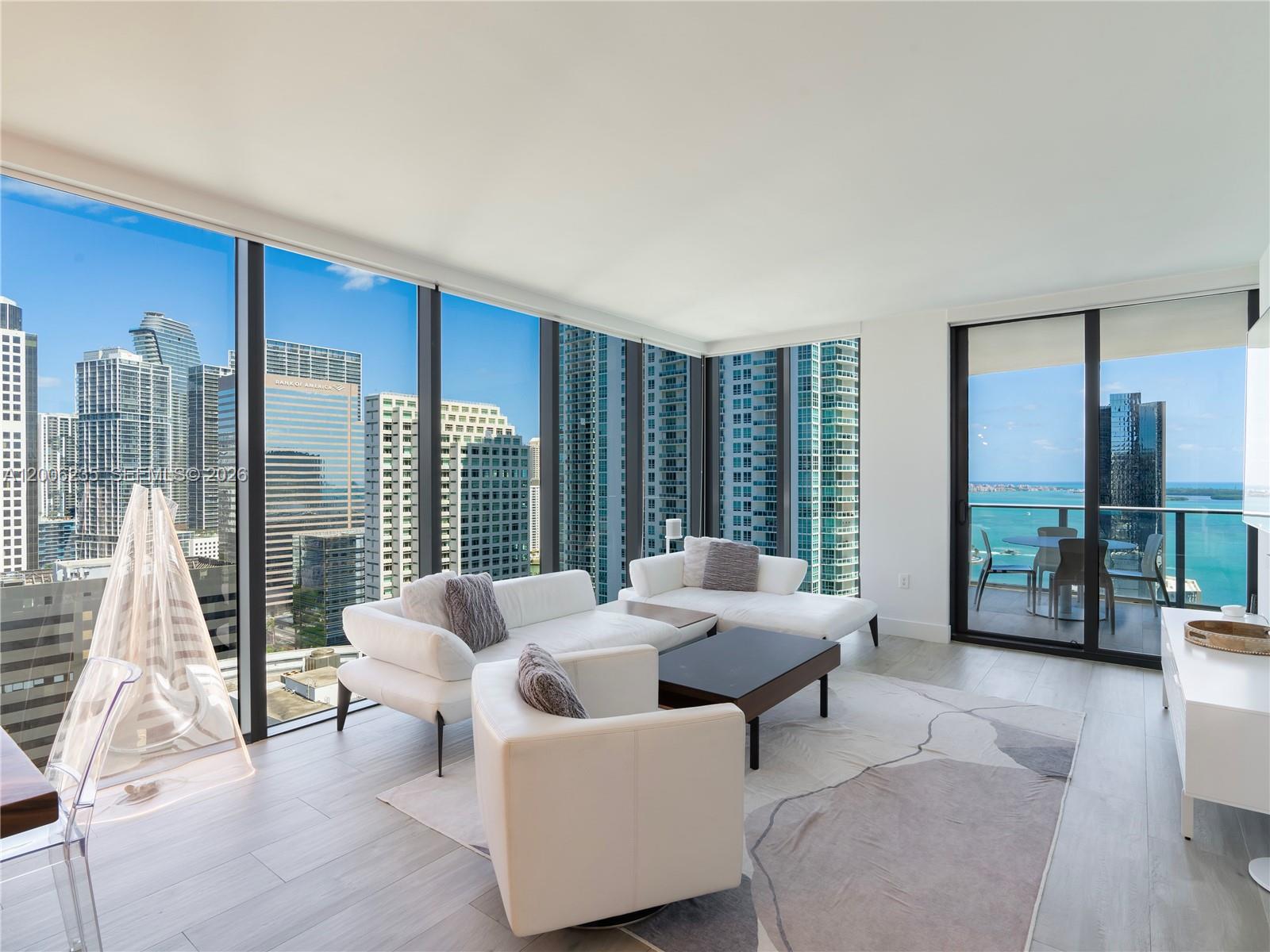 A modern living room features white sofas, a patterned rug, and floor-to-ceiling windows overlooking a city — 1010 Brickell Ave # 2801, Miami FL 33131, MIAMI, FL