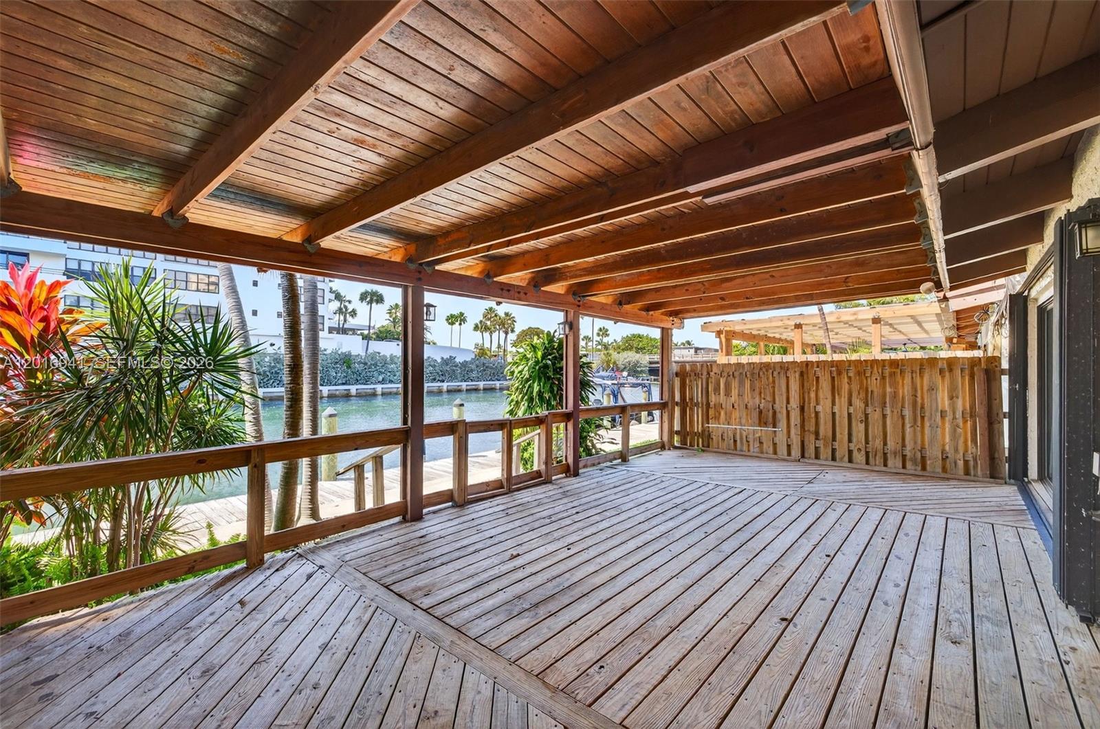 A covered wooden deck overlooks a canal with a wooden fence and palm trees — 2619 S Parkview Dr, Hallandale Beach FL 33009, HALLANDALE BEACH, FL