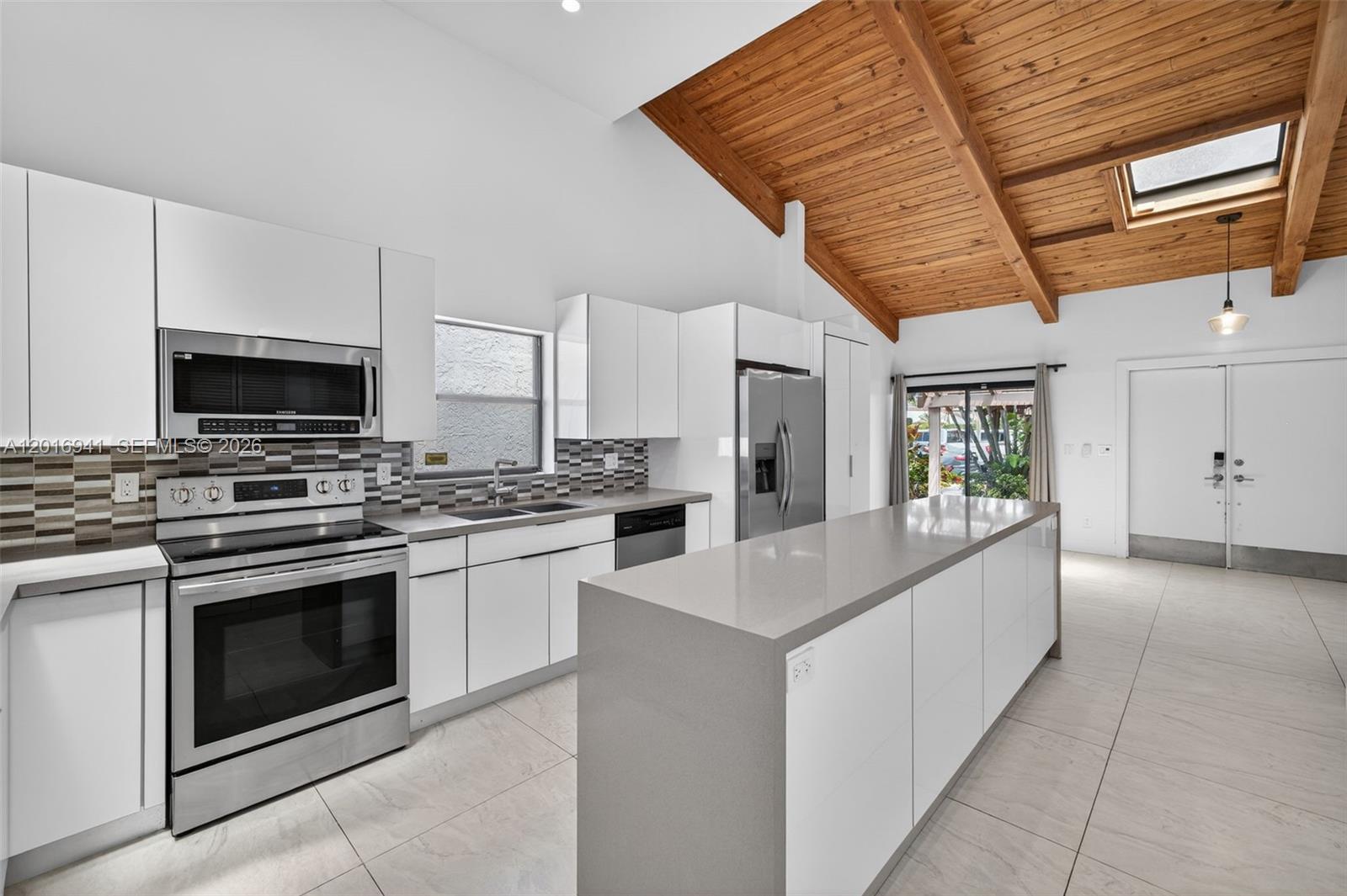 A modern kitchen features white cabinets, stainless steel appliances, a gray island, and vaulted ceilings — 2619 S Parkview Dr, Hallandale Beach FL 33009, HALLANDALE BEACH, FL