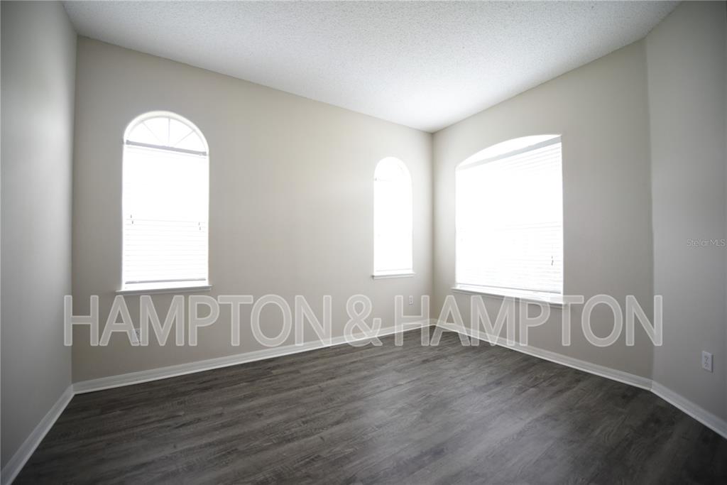 An empty room with gray wood-look flooring, light walls, and three windows — 2809 EAGLE CLAW COURT, KISSIMMEE, FL