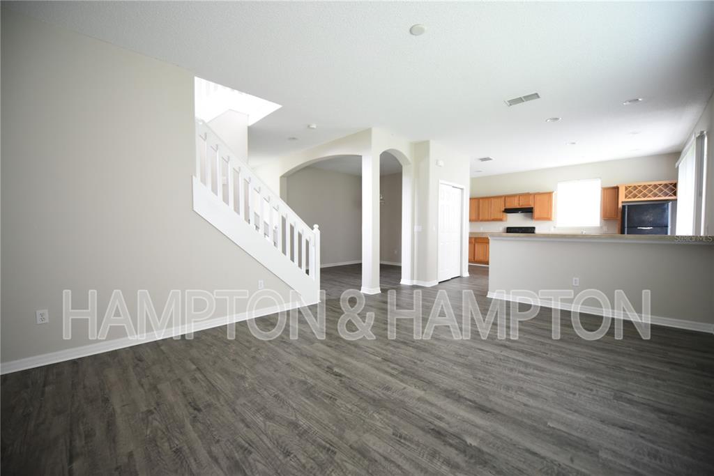 An open-concept living area features gray wood-look flooring, a white staircase, and a kitchen — 2809 EAGLE CLAW COURT, KISSIMMEE, FL